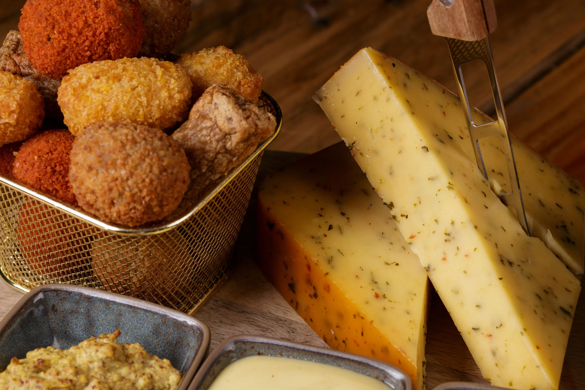 Crispy snacks, seasoned cheese, and two dips on a wooden surface.