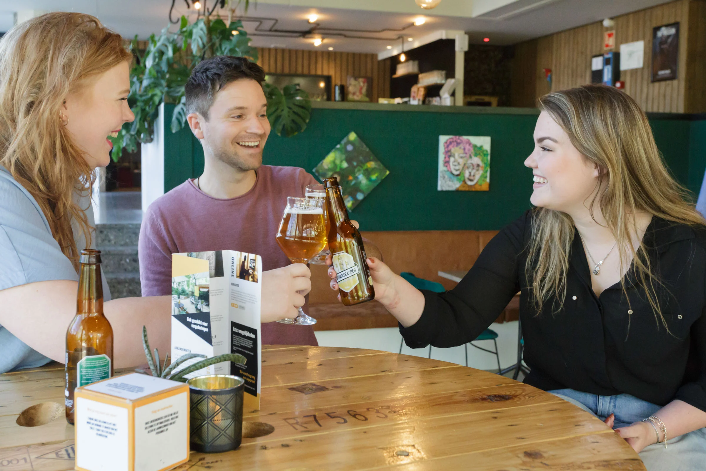 Three people cheering with beer in a cozy café.