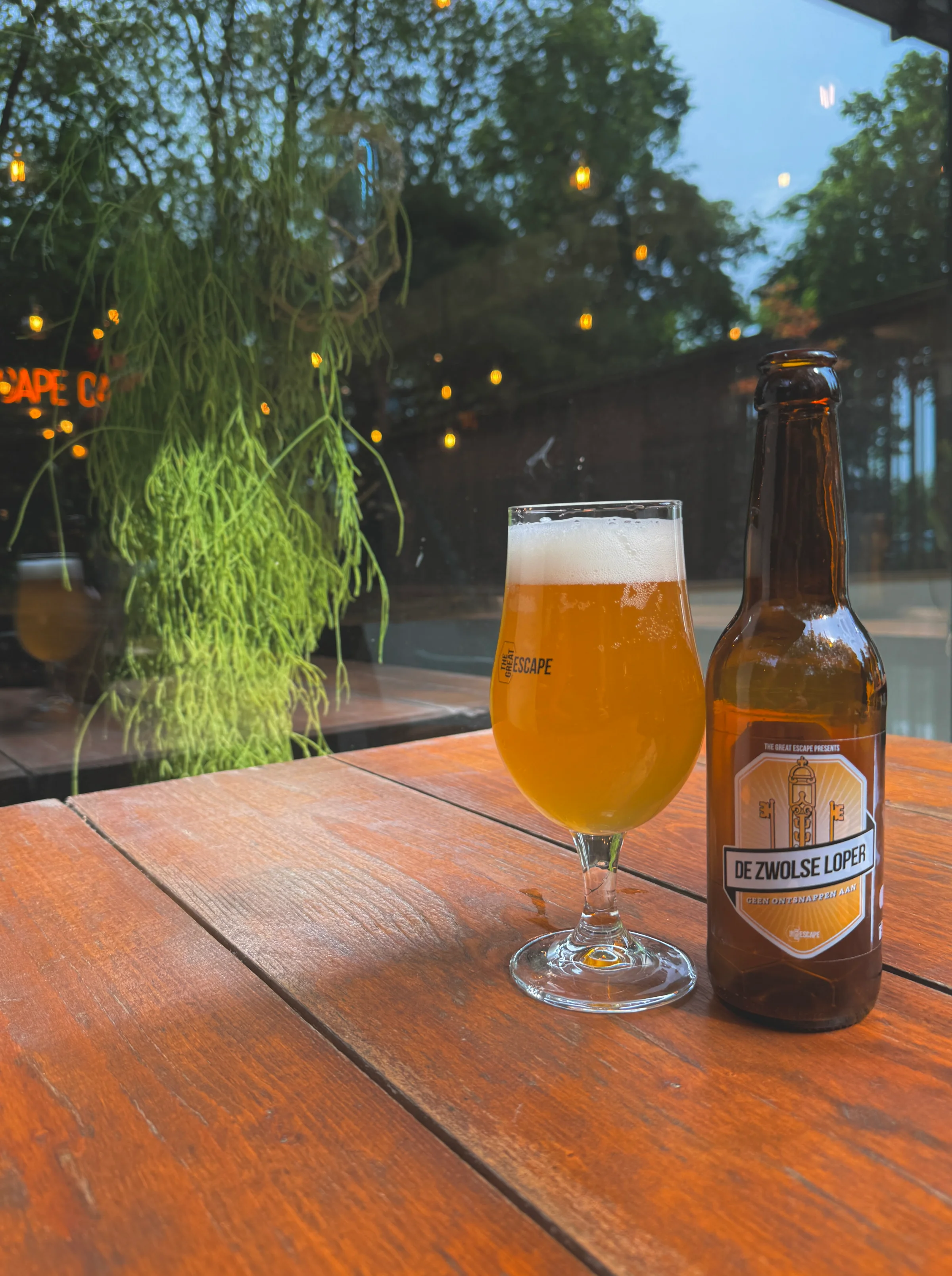 Bottle and glass of Zwolse Loper beer on a wooden terrace table.