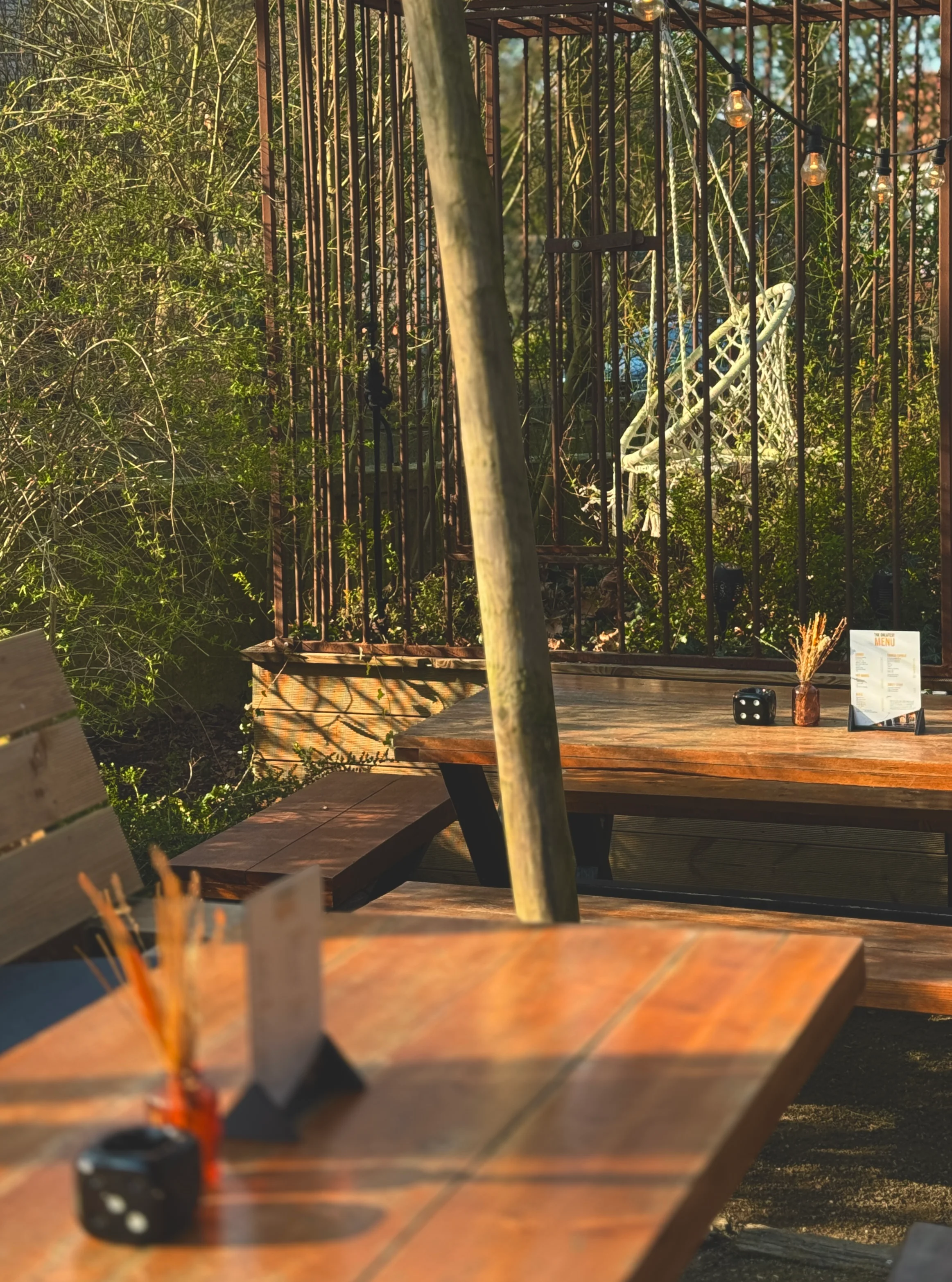 Atmospheric terrace with wooden picnic tables, plants, and birdcage decor.